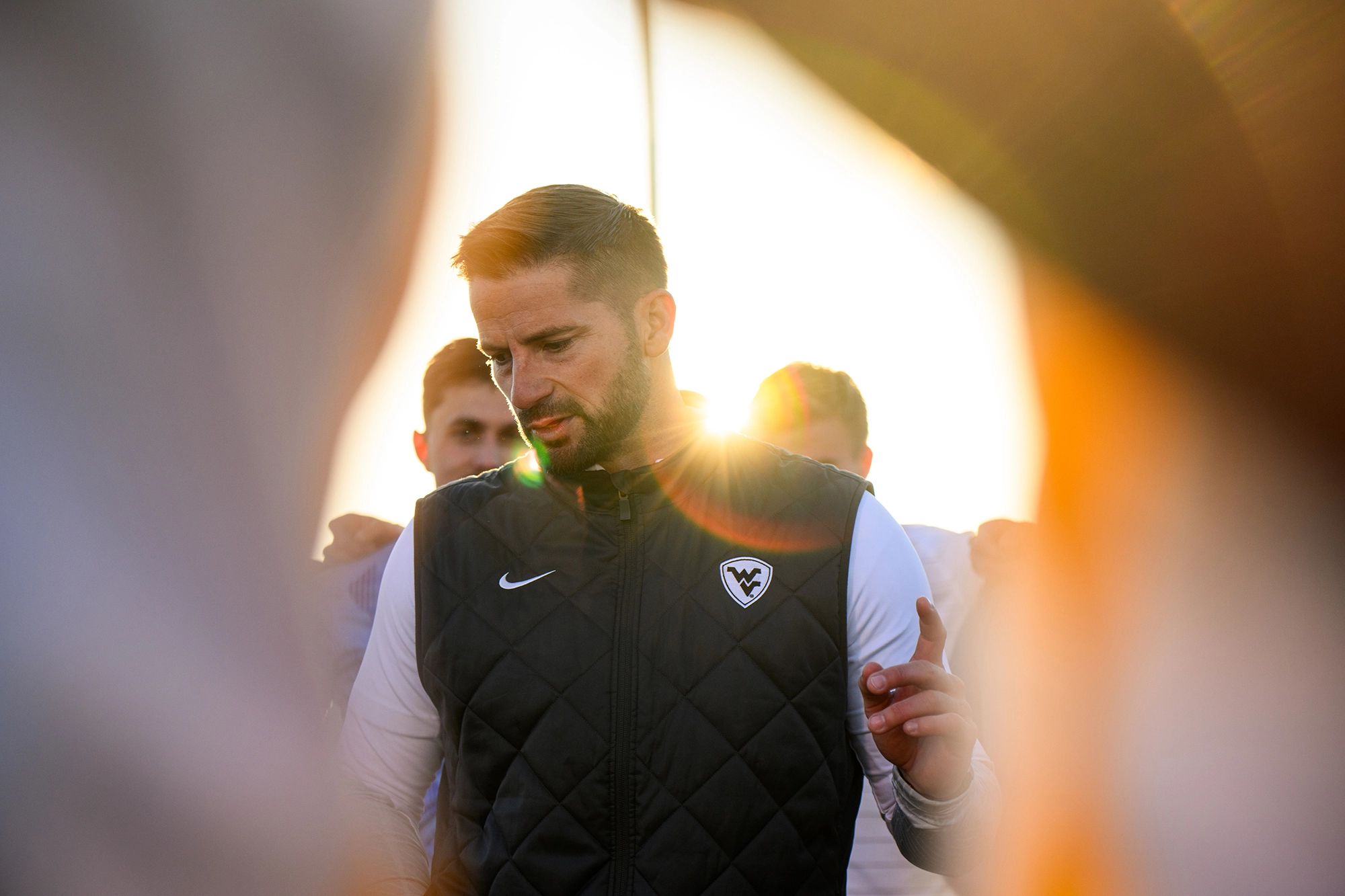 WVU Men's soccer coach in a huddle at sunset.